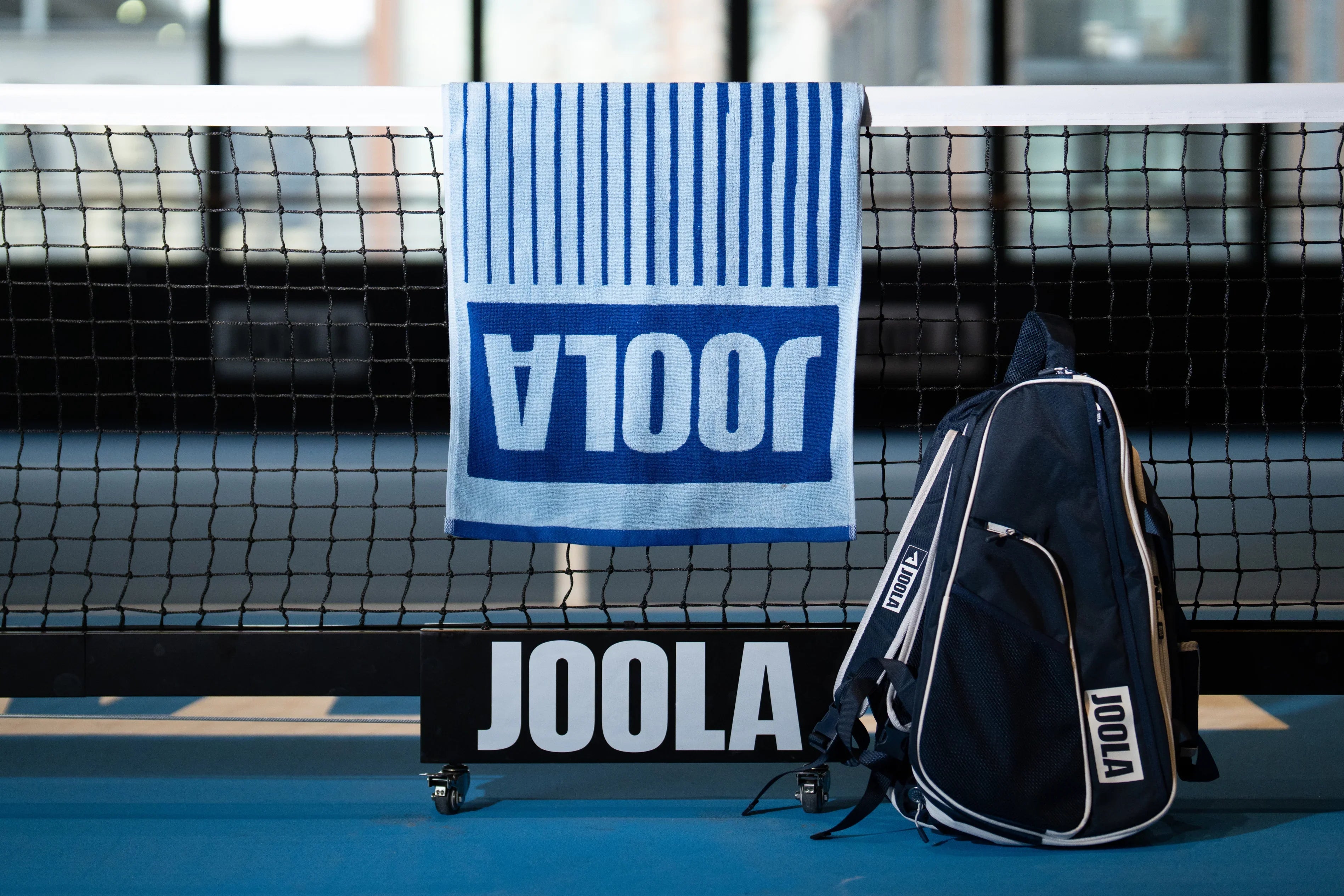 JOOLA paddle bag, towel, and net on an indoor court